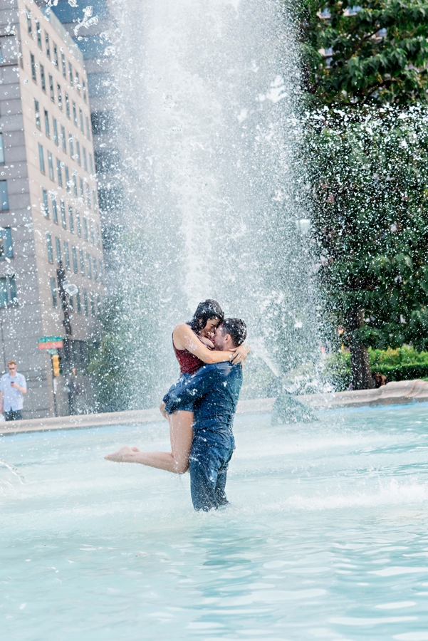 A man lifts his bride to be in the fountain at logan circle.